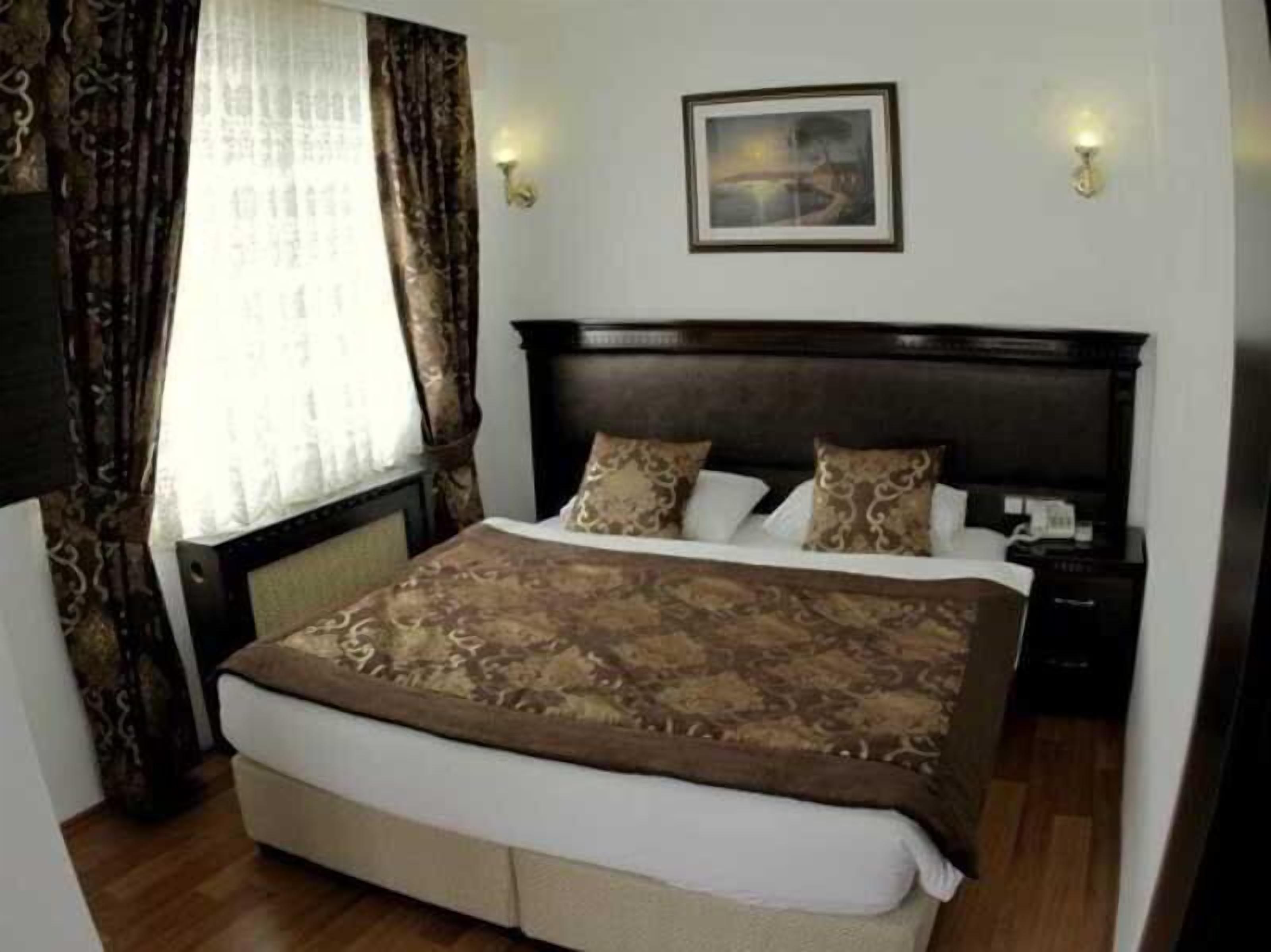A bedroom with a large bed, a nightstand, a wall-mounted lamp, and a painting on the wall.