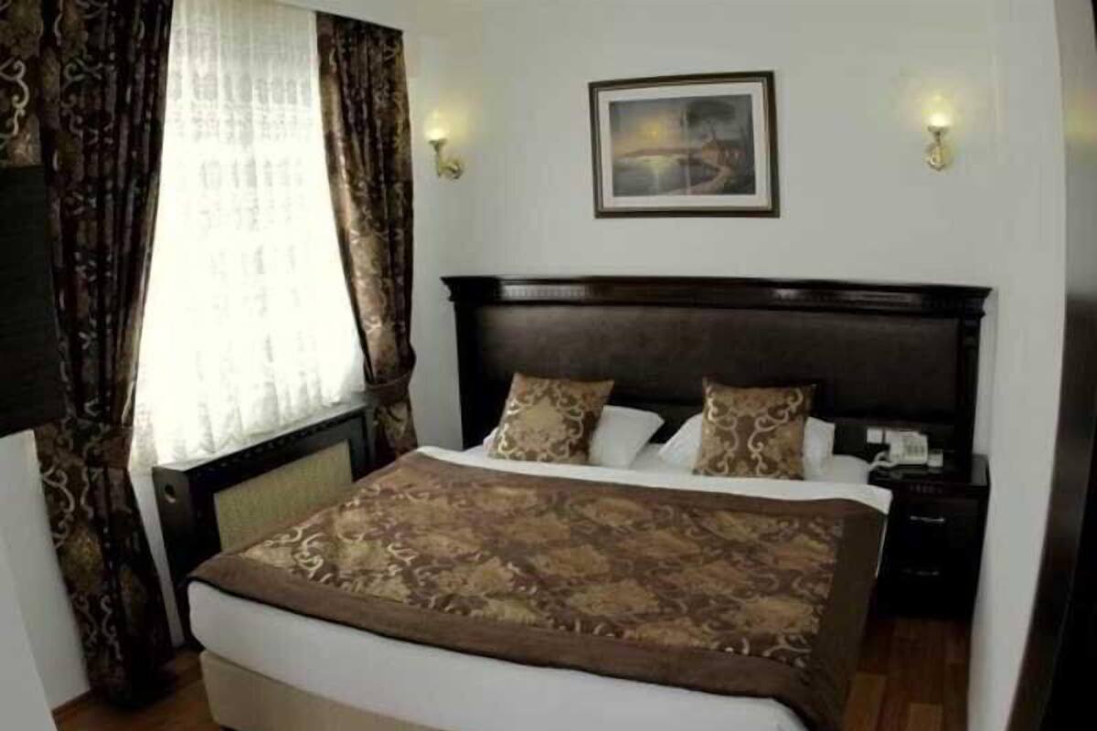 A bedroom with a large bed, a nightstand, a wall-mounted lamp, and a painting on the wall.