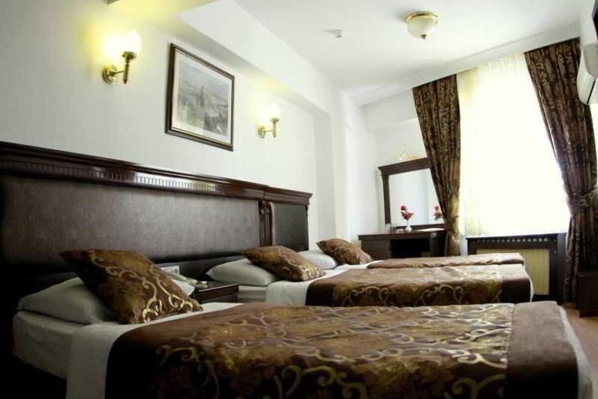 A hotel room with two beds, a wooden headboard, a large mirror, and a window with curtains.