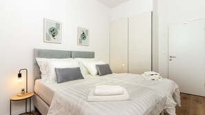 Un dormitorio moderno con cama, mesita de noche, lámpara y dos cuadros enmarcados.