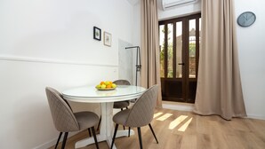 Comedor con mesa de vidrio, dos sillas, frutero, reloj en la pared y puerta corrediza de cristal.