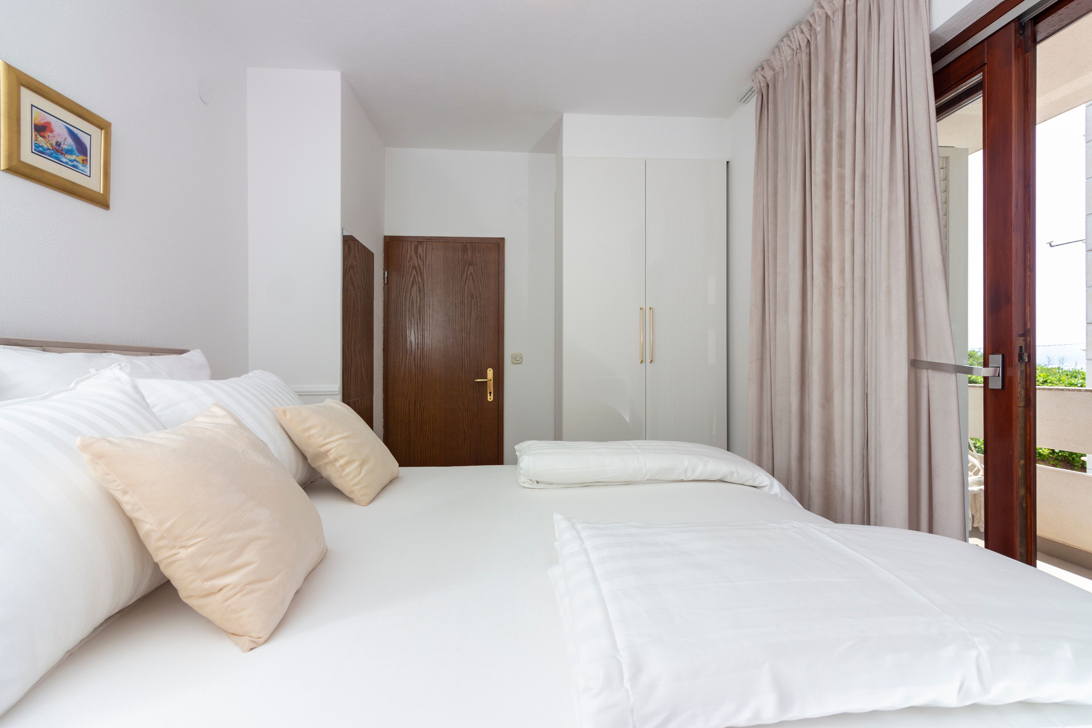 Een hotelkamer met een bed, kussens, een houten deur en uitzicht door een glazen deur.