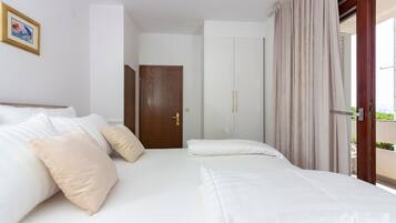 Een hotelkamer met een bed, kussens, een houten deur en uitzicht door een glazen deur.