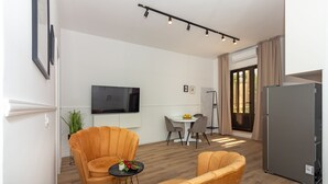 Una sala de estar moderna con un sofá, un comedor con mesa y sillas, un televisor de pantalla plana montado en la pared y un refrigerador.