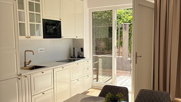 Una cocina moderna con armarios blancos, horno empotrado y un comedor con mesa y sillas de vidrio.