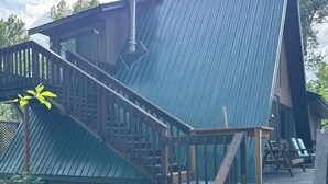 Eine rustikale Holzhütte mit einem steilen, metallenen Satteldach, einer Holztreppe und einer Terrasse mit Sitzgelegenheiten.