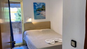 A bedroom with a bed, a painting of a beach scene, a door leading to an outdoor area, and a wall-mounted light fixture. - Villa Chalet Benidorm -  Private pool, AirCon, Walk to city centre and beaches (Benidorm)