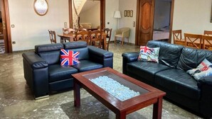 A living room with two black leather sofas, a wooden coffee table, and a dining area with wooden chairs and a table. - Villa Chalet Benidorm -  Private pool, AirCon, Walk to city centre and beaches (Benidorm)