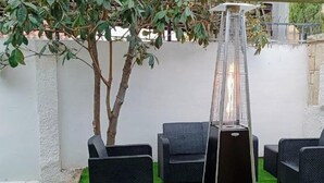 A patio with a black heater, four grey chairs, and a small tree. - Villa Chalet Benidorm -  Private pool, AirCon, Walk to city centre and beaches (Benidorm)