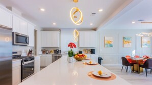 A modern kitchen with white cabinetry, a central island, and a dining area with a round table and chairs. - Amazing 5-bedroom house with AC in charming Las Vegas (Las Vegas)