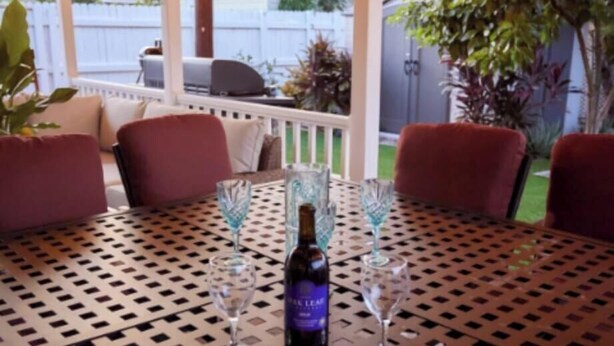 Een overdekt terras met eethoek voor twee personen, met een fles wijn, glazen en een fruitschaal.