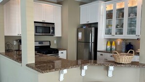 A kitchen with white cabinets, a stainless steel refrigerator, a microwave, and a granite countertop.