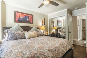 Une chambre à coucher avec un grand lit, un ventilateur de plafond, un tableau et un miroir.