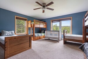 Ein Zimmer mit Etagenbetten, einem Babybett und einem Deckenventilator.