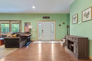 A spacious living room with a wooden floor, a sofa, a coffee table, and a fireplace. - Spacious 9BR Catskills Retreat • Views + Game Room (Andes)