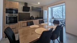 A modern kitchen with built-in appliances, a dining area with a wooden table and chairs, and a large window providing natural light.