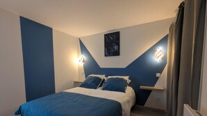 A bedroom with a bed, two bedside lamps, a nightstand, and a wall-mounted light fixture.