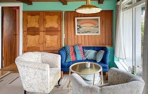 A cozy room with a blue sofa, patterned armchairs, a wicker table, and wooden paneling. - Gorgeous home in Børkop with WiFi (Børkop)