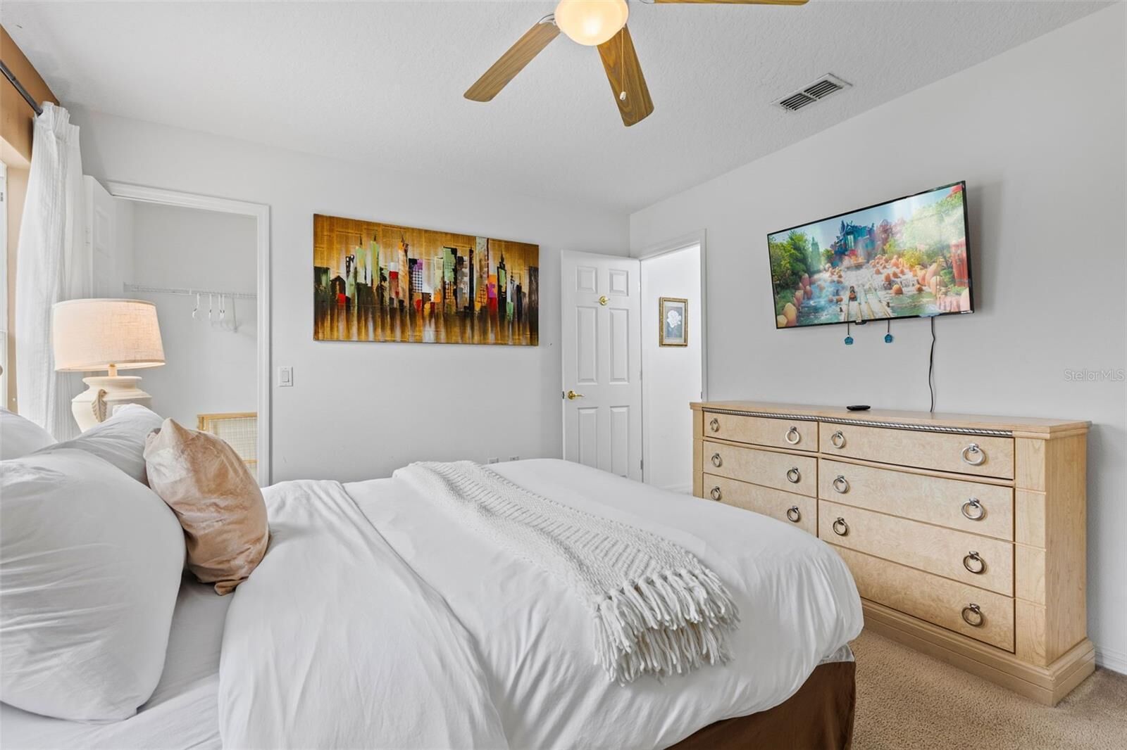 Une chambre à coucher avec un lit, une commode, un ventilateur de plafond, un tableau et un téléviseur.