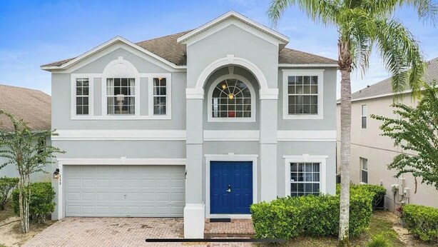 Ein zweigeschossiges Haus mit Garage, einer blauen Haustür und einem kleinen Vorgarten mit einer Palme.