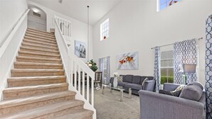 Eine Treppe führt zu einem Essbereich mit einem grauen Sofa und gemusterten Vorhängen.