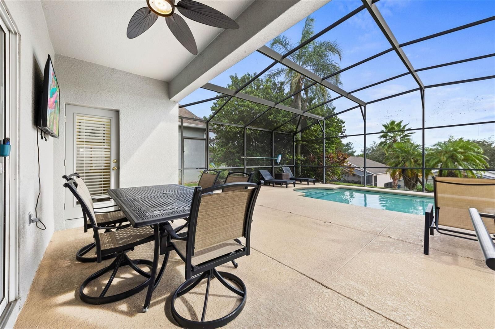 An outdoor patio with a pool, a table with chairs, and a ceiling fan.