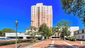 A multi-story building with a flat facade, a parking area with a 'No Parking' sign, and a clear blue sky.