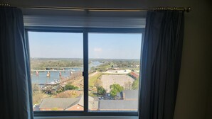 A room with a large window overlooking a bridge, a parking lot, and a body of water.