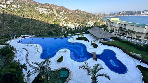 Ett semesterparadis med en stor, slingrande pool omgiven av palmer och med utsikt över havet.