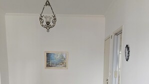 Ett vardagsrum med en grå lädersoffa, en trästol, en grön hopfällbar stol, en inramad tavla på väggen och en taklampa.