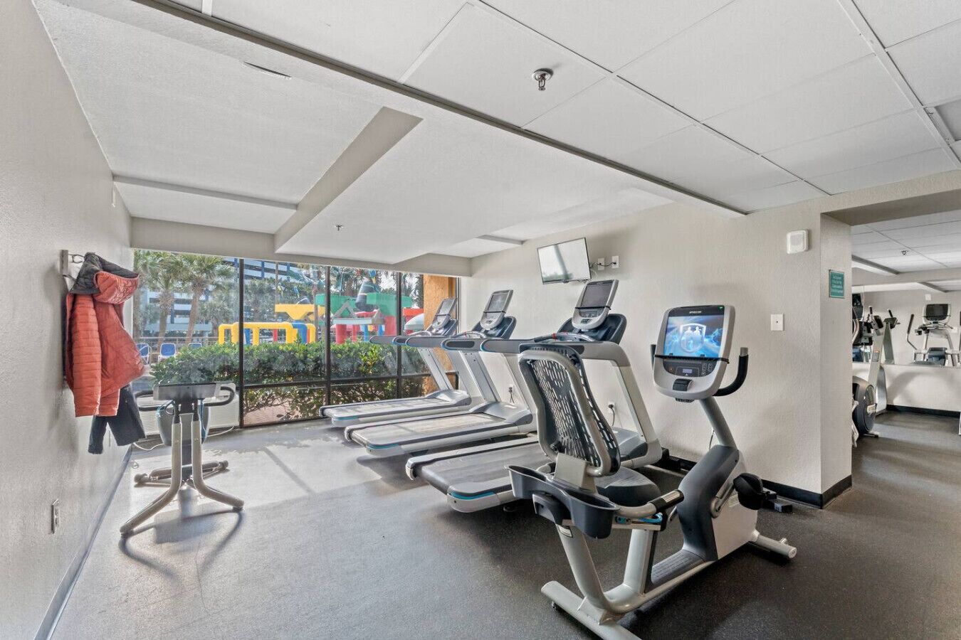 A gym with treadmills, exercise bikes, and a view of outdoor playgrounds.