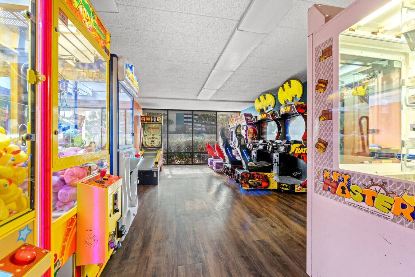 A row of arcade games with plush toys and a Batman-themed machine.