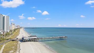 A beach with a pier extending into the ocean, adjacent to a cityscape with high-rise buildings.