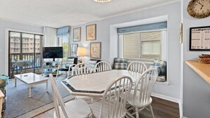 A dining area with a white table and chairs, a television, and framed artwork on the walls. - Beachfront Resort Condo with Pools and Hot tub (North Myrtle Beach)