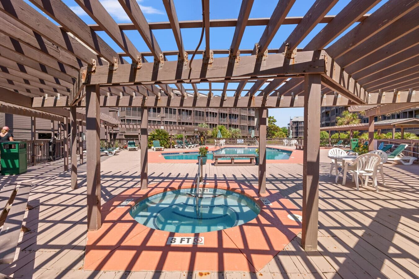Un'area piscina esterna coperta con una pergola in legno, diverse piscine e lettini da relax.