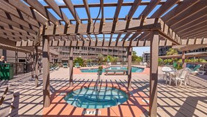 A covered outdoor swimming pool area with a wooden pergola, multiple pools, and lounge chairs. - Beachfront Resort Condo with Pools and Hot tub (North Myrtle Beach)