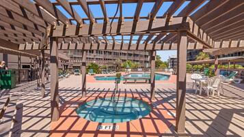 A covered outdoor swimming pool area with a wooden pergola, multiple pools, and lounge chairs.