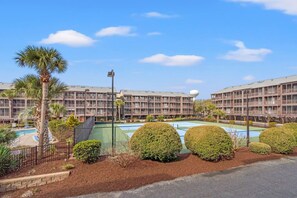 Ein Hotel mit mehreren Etagen, einem Schwimmbad und gepflegter Bepflanzung.