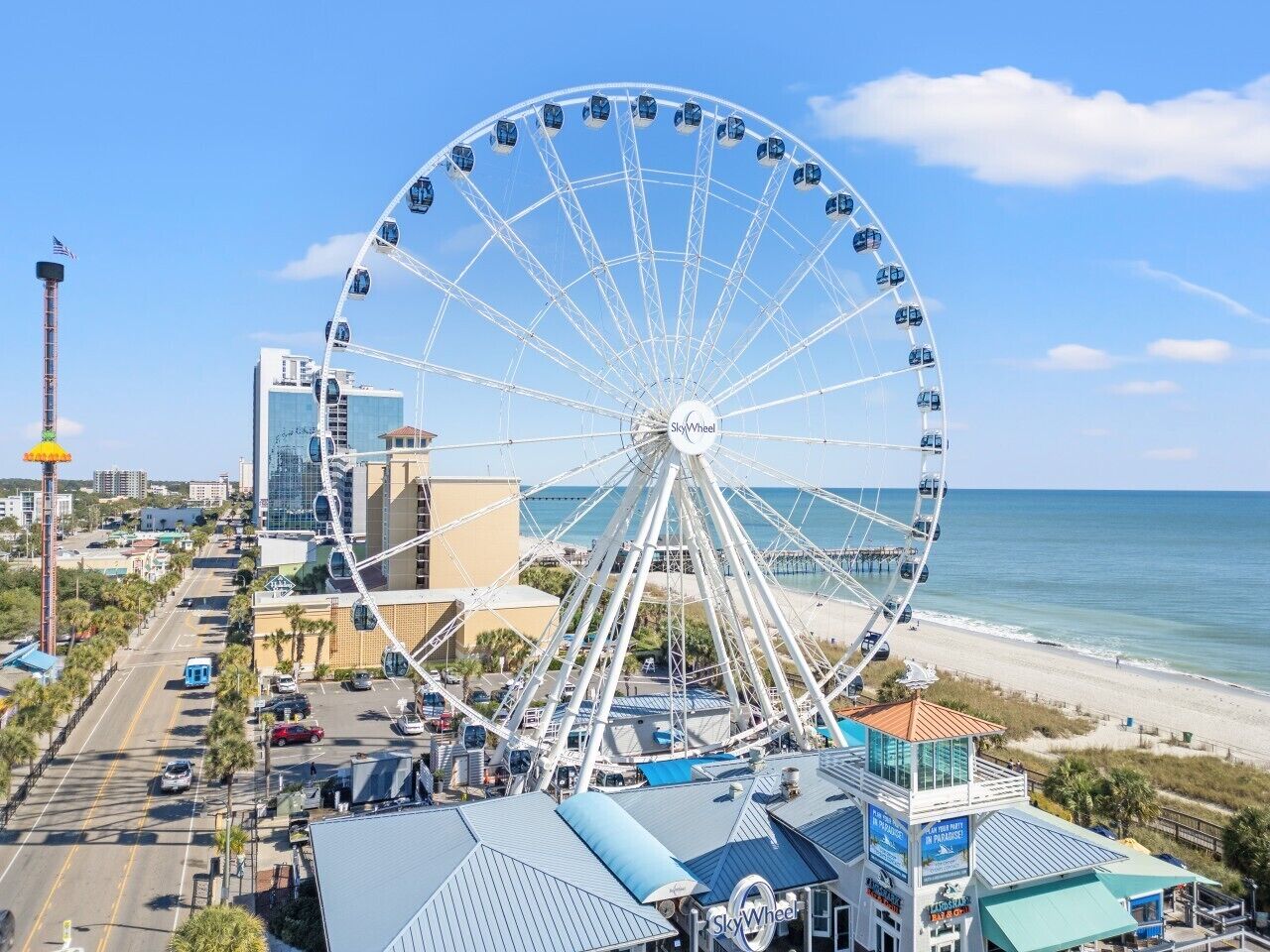 A large Ferris wheel with cabins, a beach, and a cityscape with modern buildings.