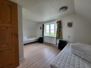 Et værelse med dør i træ, et vindue med gardiner, en radiator, en seng og et lille bord.