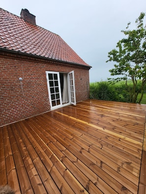 Una casa de ladrillo con techo de tejas rojas y terraza de madera.