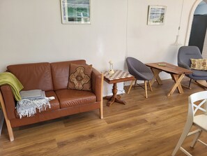 En stue med en brun lædersofa, et lille træbord, en grå lænestol og en hvid stol.