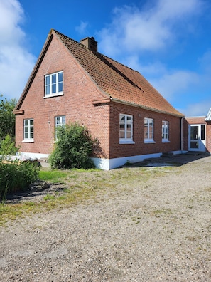 Ein rotes Backsteinhaus mit geneigtem Dach, weißen Fensterrahmen und einer Schotterauffahrt.