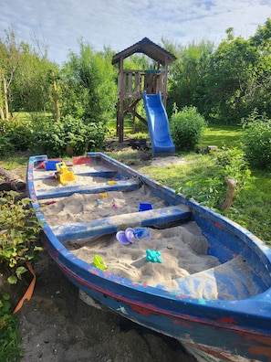 Un'area giochi sabbiosa con uno scivolo e una struttura in legno.