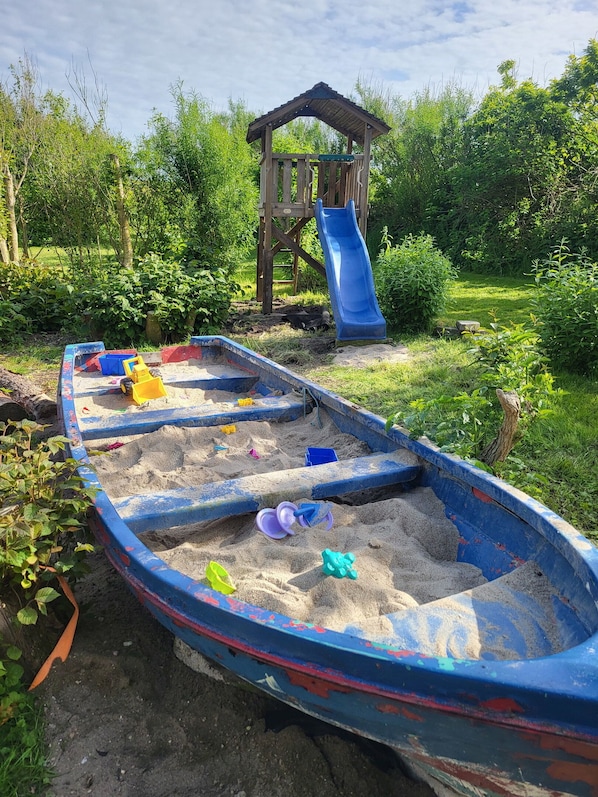 Ein Sandspielplatz mit Rutsche und einer Holzkonstruktion.
