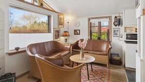 Ein gemütliches Zimmer mit Korbmöbeln, einem runden Tisch mit einer Vase, einer Uhr und einem Fenster mit Jalousien.