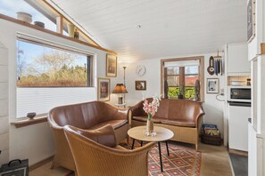 A cozy room with wicker furniture, a round table, and a view of trees through a window. - Lovely holiday home near sandy beach (Vig)