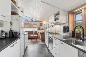A modern kitchen with white cabinetry, a black countertop, and a window overlooking a garden. - Lovely holiday home near sandy beach (Vig)