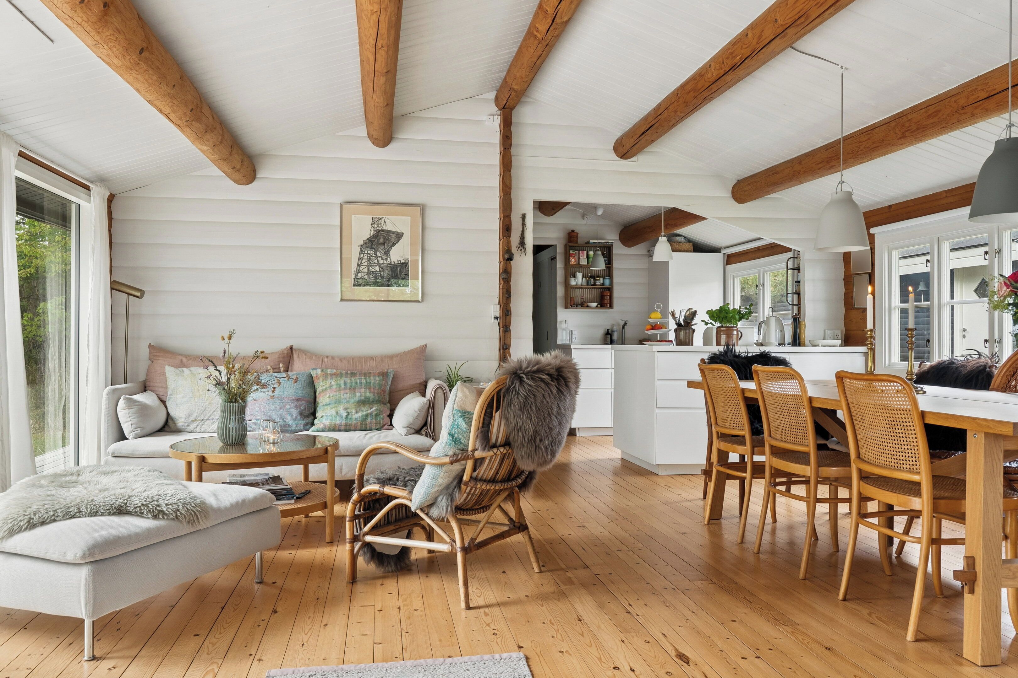 A spacious living area with a wooden ceiling, a sofa with decorative pillows, a wicker chair, and a dining table with chairs.