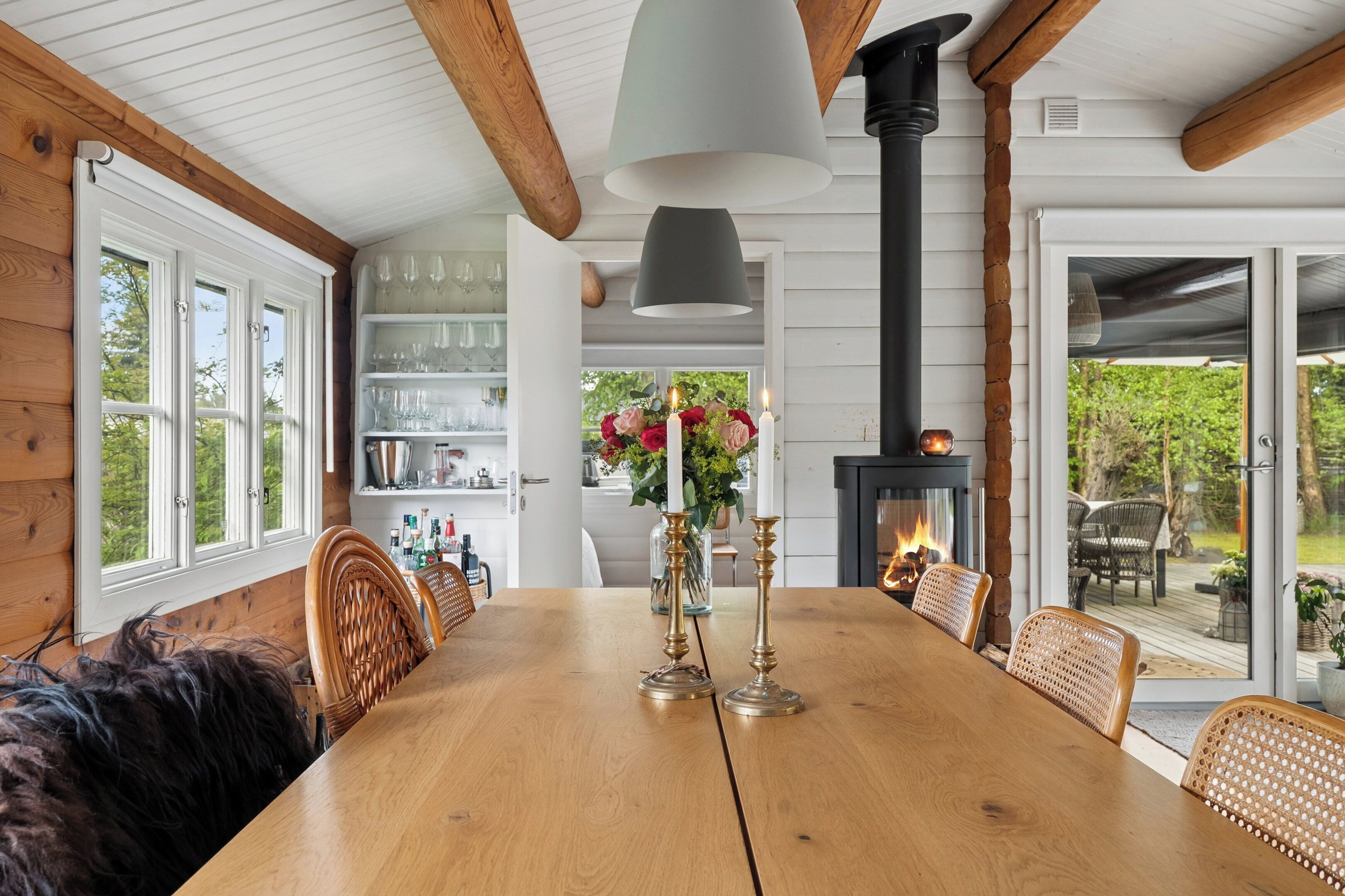 Una mesa de madera con sillas, un florero con flores y una chimenea.